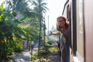Sri Lanka 'nın dağlık bölgelerindeki çay tarlaları arasında Ella' dan Kandy 'ye tren yolculuğunun tadını çıkaran genç bir kadın.