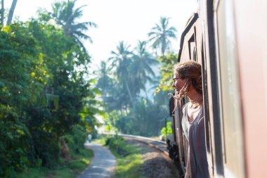 Sri Lanka 'nın dağlık bölgelerindeki çay tarlaları arasında Ella' dan Kandy 'ye tren yolculuğunun tadını çıkaran genç bir kadın.