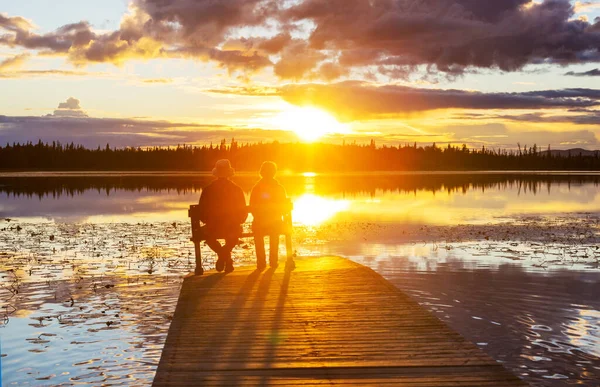 Couple resting at ease by the calm lake at sunset. Relaxation vacation