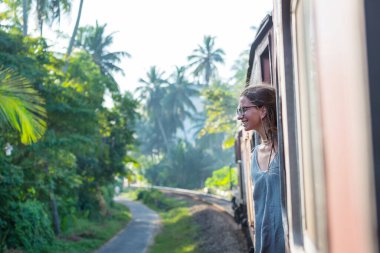 Sri Lanka 'nın dağlık bölgelerindeki çay tarlaları arasında Ella' dan Kandy 'ye tren yolculuğunun tadını çıkaran genç bir kadın.