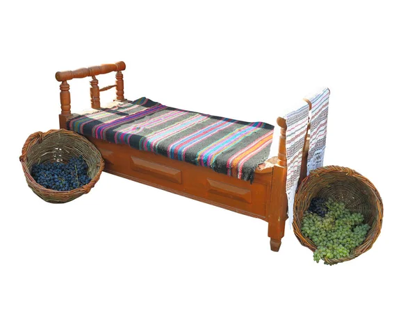 白色底座上有地毯和葡萄篮的老式木制古董床 — 图库照片
