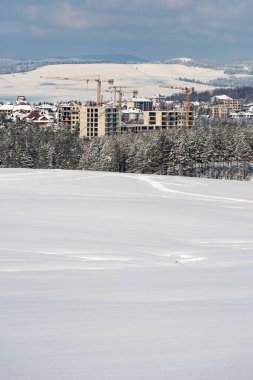 İnşaat endüstrisi apartmanı ve Zlatibor 'daki konut geliştirmesi kış mevsiminde kar altında, bina ve vinçler çam ormanlarını ele geçiriyor.
