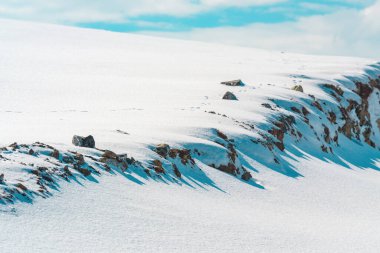 Kış mevsimi manzarası, arka planda mavi gökyüzü ve bembeyaz karla kaplı bir dağ tepesi.