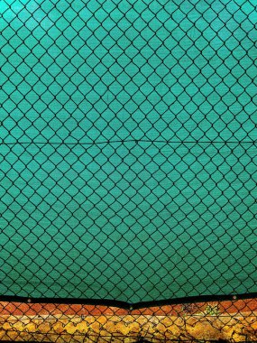 Chain-link fencing with the diamond pattern and green fiber screening as background