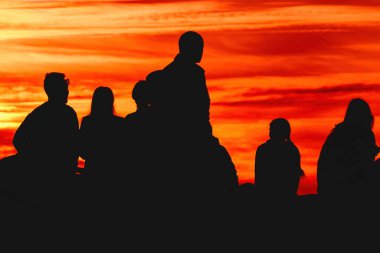 Back lit group of people in silhouette enjoying amazing summer sunset with orange sky in background