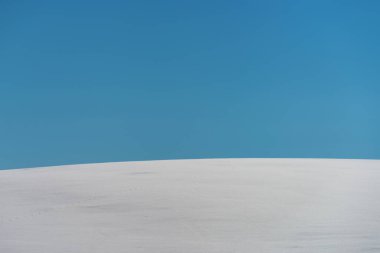 Abstract minimalistic winter landscape, snow covered hill with blue sky in background on sunny day, copy space included