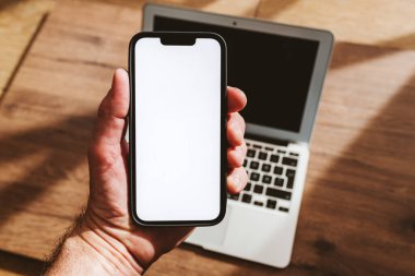 Akıllı telefon modeli, elinde cep telefonu olan, dizüstü bilgisayarında beyaz ekran olan, seçici odaklı bir adam.