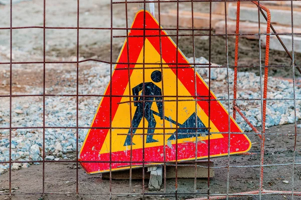Men at work sign behind the steel wire fence on construction site, selective focus