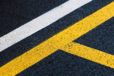 Bir otoparkın yepyeni asfalt yüzeyinde yol işaretlemesi, soyut arka plan olarak sarı ve beyaz çizgiler