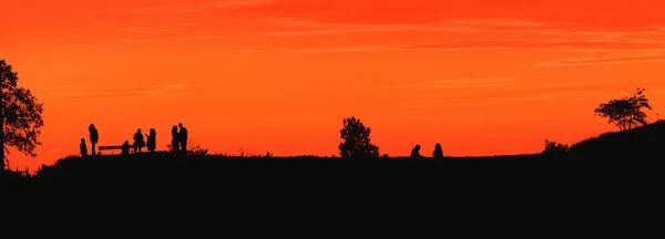 在背景为橙色天空的山丘上欣赏风景和夏日落日的一群难以辨认的人的轮廓 — 图库照片