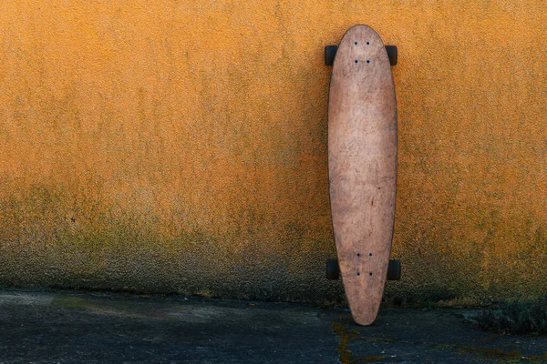 汚れたオレンジ色の壁にもたれて着用スケートロングボード 選択的な焦点 — ストック写真
