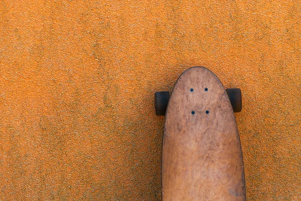 汚れたオレンジ色の壁にもたれて着用スケートロングボード 選択的な焦点 — ストック写真