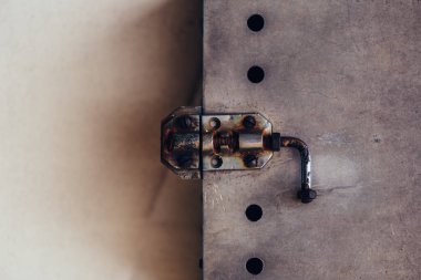 Eski paslı kapı sürgüsü yıpranmış metalik kapı koluna takılmış.