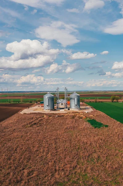 Farm silos in field, aerial view from drone pov on sunny spring day with white clouds over horizon