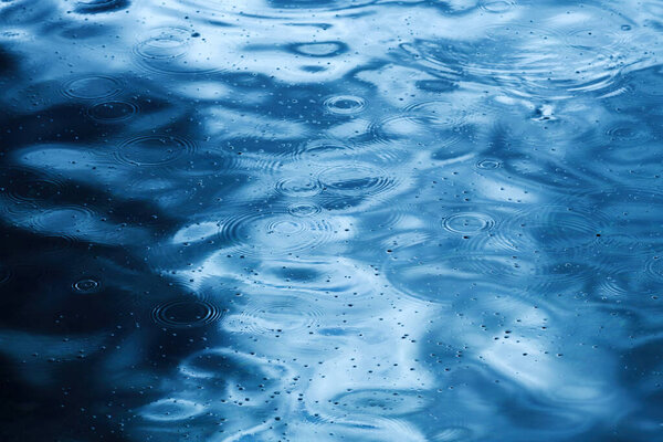 Rain drop circular pattern on rippled blue water surface, raindrops circles as abstract seasonal background, selective focus