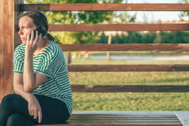 Cep telefonundan arayan bir kadın, halka açık bir parkta telefona cevap vermiyor, seçici bir odaklanma.