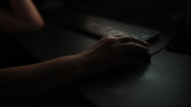 Woman using desktop computer mouse in dark home office interior, closeup of hands with selective focus