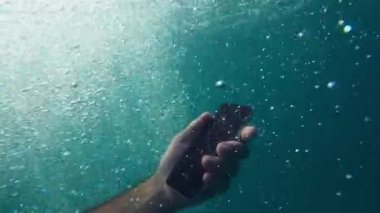 Yaz tatili sırasında derin mavi denizde sualtında akıllı telefon kullanan bir adam seçici bir şekilde odaklanır.