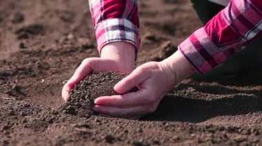 Bir avuç verimli toprak, çiftçi ellerindeki toprağı sürüyor ve tohumlama sezonundan önce kalitesini kontrol ediyor, seçici odaklı yavaş çekim.