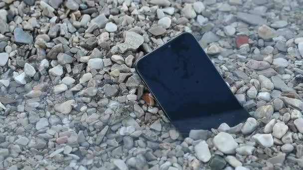 夏日早上在海滨海滩的卵石中丢失的智能手机装置 有选择地聚焦 — 图库视频影像