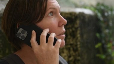 Yağmurda dışarıda cep telefonuyla konuşan yetişkin kadın portresi, seçici odaklanma