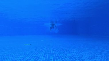 Kapalı yüzme havuzunda yüzen bir erkeğin sualtı görüntüsü, düşük açı.