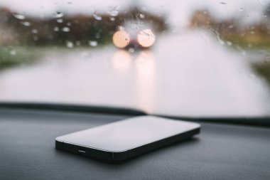 Yağmurlu bir günde araba panelindeki akıllı telefon, seçici odaklanma