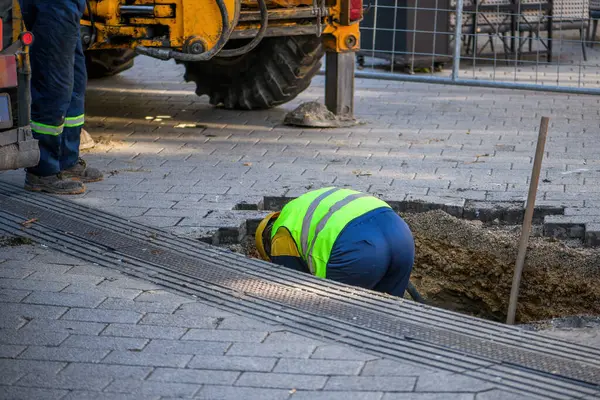 通りの舗装の下で損傷した水管を修理する現場のメンテナンス労働者 選択的な焦点 — ストック写真