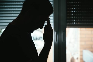Depresyon ve üzüntü, akıl sağlığı konsepti. Pencerenin kenarında kepenkleri indirilmiş umutsuz bir erkek silueti. Seçici odak.