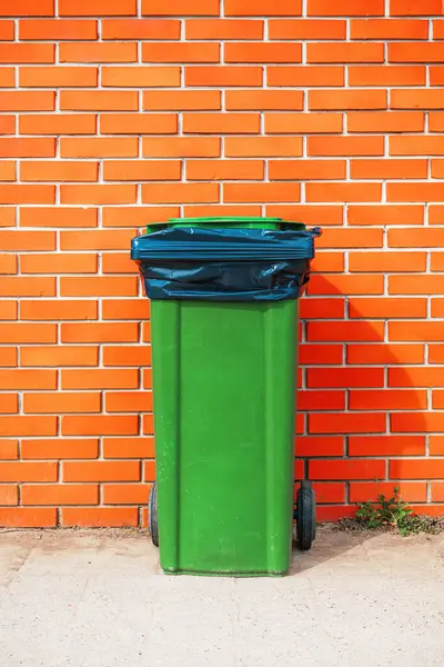 Green plastic garbage can against orange brick wall, copy space included