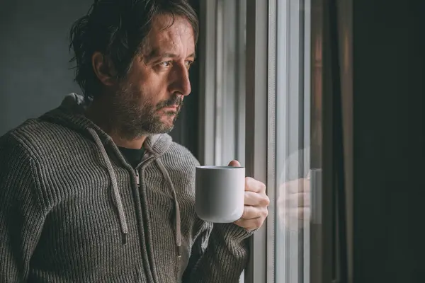 多愁善感的成年男子早上在公寓窗边喝咖啡 一边朝外看一边想 开始新一天的咖啡因用量 有选择的重点 — 图库照片