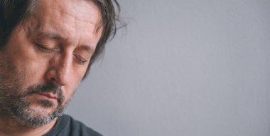 Yorgun, uykulu bir adam başını duvara yaslıyor gözleri kapalı, seçici bir şekilde odaklanıyor.