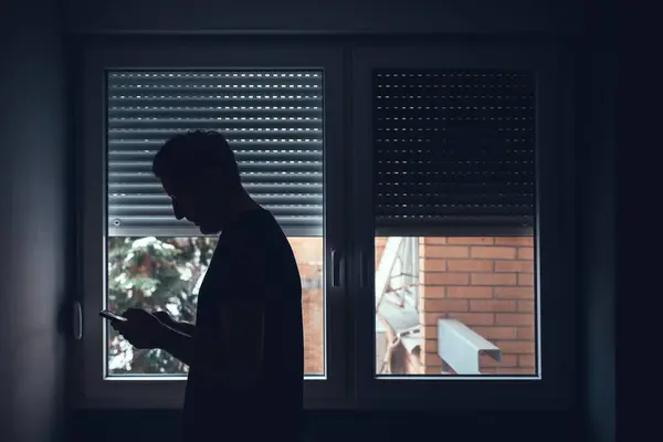 Depresyondaki Üzgün Adam Pencerenin Yanındaki Karanlık Odada Cep Telefonu Kullanıyor Telifsiz Stok Fotoğraflar