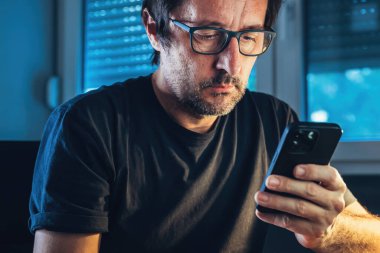 İç mekânda cep telefonu kullanan bir adam. Masada otururken akıllı telefondan mesaj yazan sıradan bir erkek. Seçici odak.