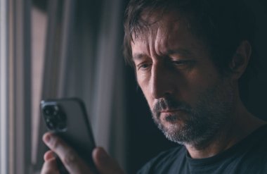 Apartman penceresinin yanında dururken cep telefonundan mesaj okuyan adam, seçici odaklanma