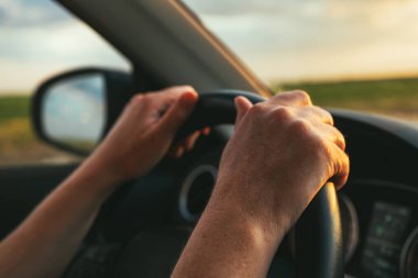 Traveling through countryside by your own car, closeup of female hands gripping the steering wheel of a modern automobile vehicle, selective focus clipart