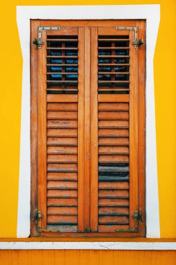 Sarı duvarda ahşap panjurları olan eski pencere, dikey görüntü