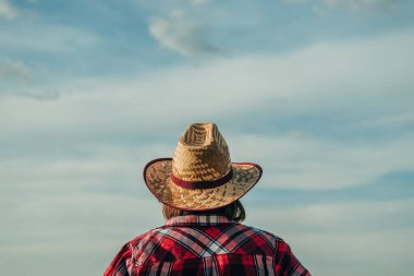 Hasır şapkalı kadın çiftçinin tarlada dikilip hasat boyunca ufka bakarken güneşli bir yaz gününde mahsul hazırlarken, seçici bir odak noktası vardı.