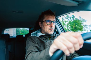 Gözlüklü dikkatli sürücü, arabayı sürerken yola dikkatlice bakıyor, seçici odaklı.