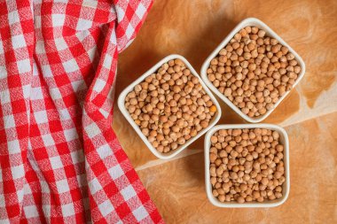 Masanın üstünde kırmızı kareli bezelye ile üç kase nohut.