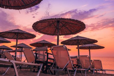 Yunanistan 'ın Vrasna plajında yaz gündoğumunda Palapa sazlık güneş şemsiyeleri. Seçici odak.