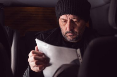 Gece arabanın arka koltuğunda otururken ciddi ciddi mektup okuyan düşünceli bir adam, seçici bir şekilde odaklanmış.