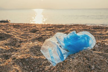 Blue plastic bag at sandy beach in summer sunrise, selective focus clipart