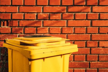 Tuğla duvara dayalı sarı plastik çöp kutusu, seçici odak