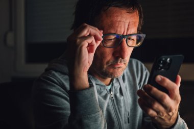 Bored man using smartphone late at night, browsing the internet or using social media apps, selective focus clipart