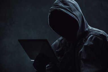 Kapüşonlu bilgisayar korsanı dijital tablet kullanıyor, seçici odak