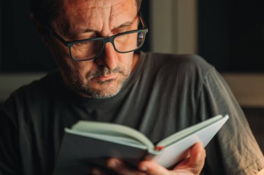 Kitap kurdu konsepti. Evde kitap okumak, gecenin geç saatlerinde yalnız başına yetişkin bir erkeğin gösterişsiz portresi, seçici bir odak noktası..