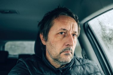 Soğuk kış gününde arabada oturan kaygılı erkek sürücü buzlu yoldaki arabanın ön camından bakıyor, seçici bir şekilde odaklanıyor.