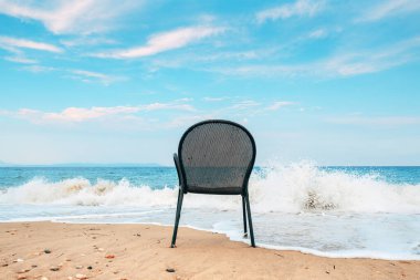 Empty metallic chair on sandy beach in Vrasna Greece. Aegean sea waves splashing the sand shoreline of Strymonic Gulf. Selective focus. clipart