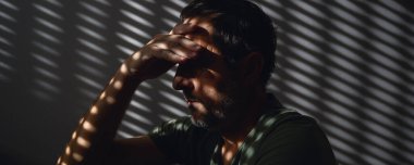 Pişmanlık. Pişman yetişkin erkek, karanlık odada yalnız oturuyor. Seçici odak.